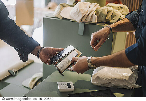 Cropped hands of male customer and clerk doing mobile payment at checkout in clothing store