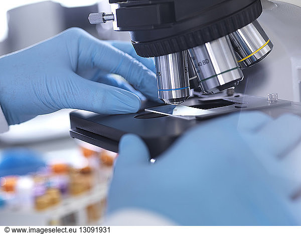 Cropped hands of male scientist analyzing blood sample through microscope in laboratory