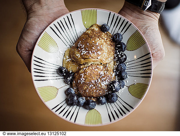 Cropped hands of man holding pancakes with grated cheese and blueberries in plate