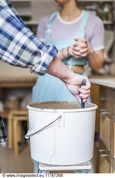 Cropped hands of mature female potter mixing clay with employee standing in background