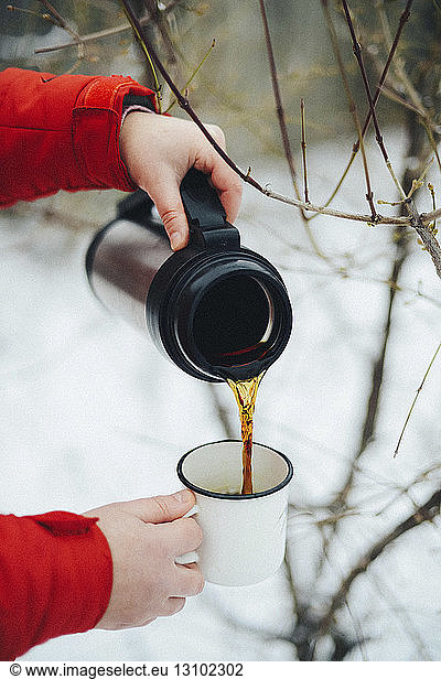 Cropped hands of woman pouring black coffee from insulated drink container into mug during winter