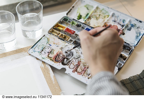 Cropped image of artist mixing watercolor paints while working in creative office