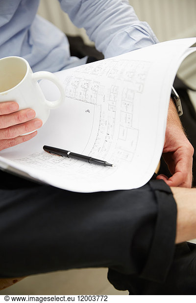 Cropped image of businessman with blueprints having coffee at creative office