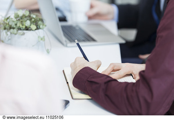 Cropped image of businessman writing in book in meeting
