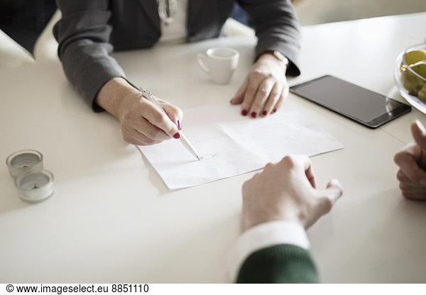 Cropped image of businesswoman drawing while explaining colleague at desk