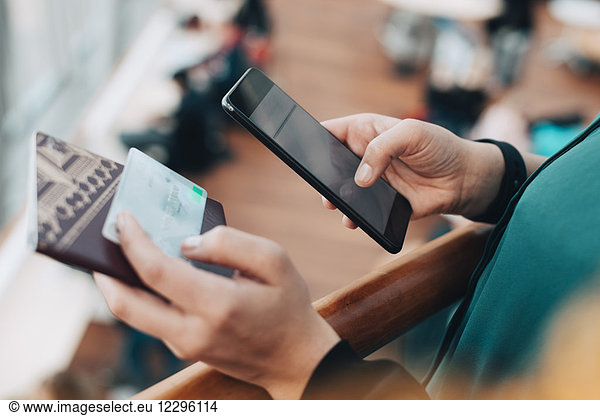Cropped image of businesswoman holding credit card while using mobile phone in airport