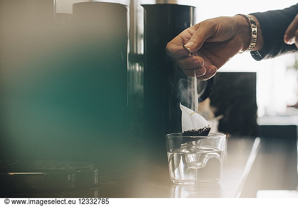 Cropped image of businesswoman making tea in drinking glass at office