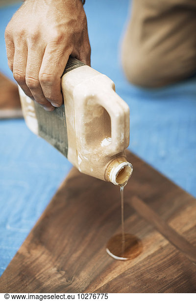 Cropped image of carpenter pouring oil on triangle shaped wood at workshop