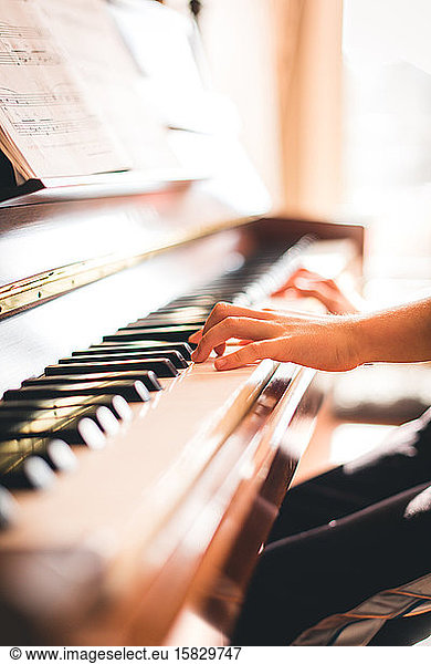 Cropped image of child's hands playing piano in a sunny room.