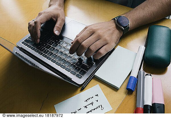Cropped image of computer programmer typing on laptop at desk in startup company