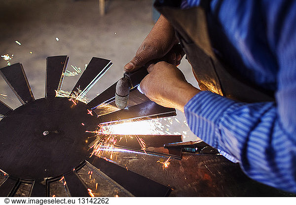 Cropped image of craftsperson welding circular metal at factory