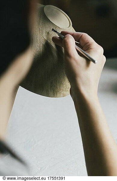 Cropped image of craftswoman painting bowl in workshop