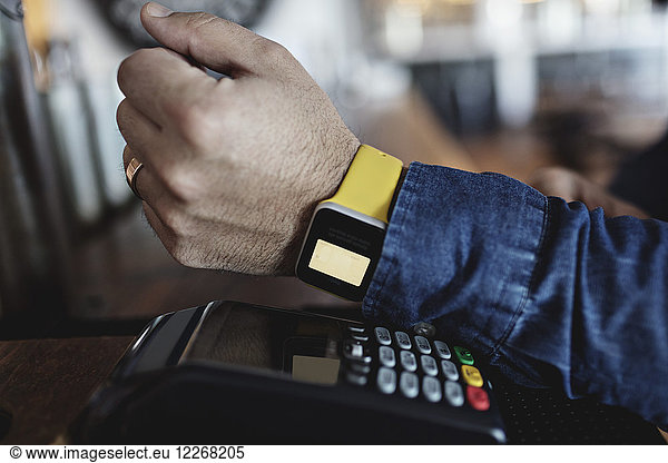 Cropped image of customer doing contactless payment through smart watch at bar counter