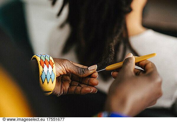Cropped image of female barber making locs with crochet hook in salon
