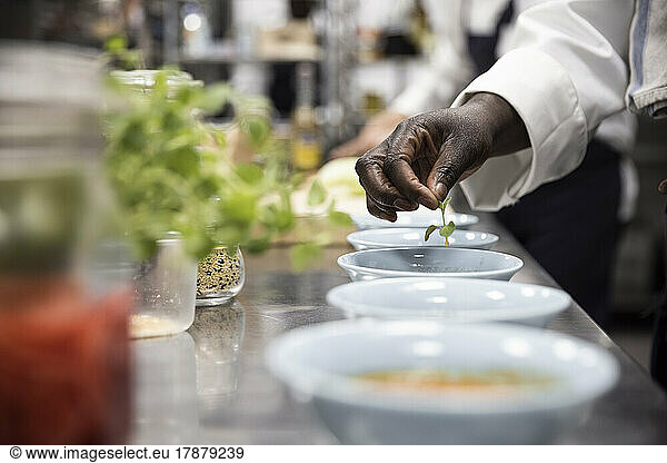Cropped image of female chef garnishing soup with basil leaf in restaurant