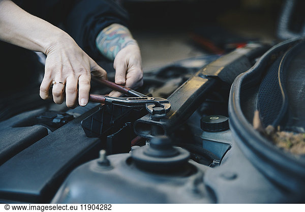 Cropped image of female mechanic tightening nut on car engine with wrench