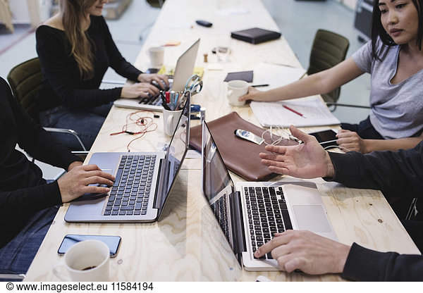 Cropped image of four people using laptop at desk in office