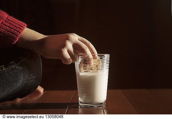 Cropped image of girl dipping cookie in milk