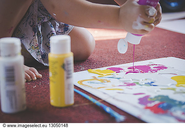 Cropped image of girl pouring watercolor paints on paper at home
