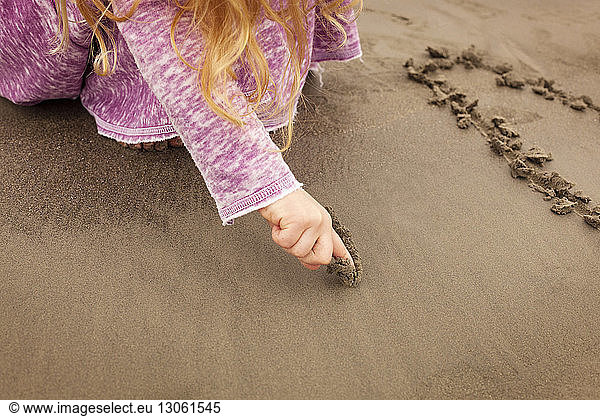 Cropped image of girl writing on sand at beach
