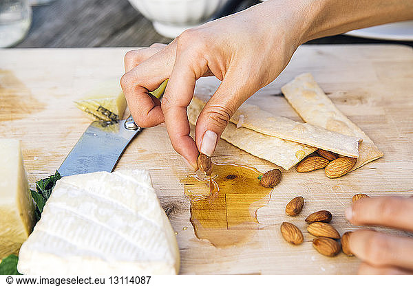 Cropped image of hand garnishing almond with honey on cheese board