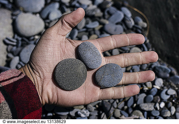 Cropped image of hand holding pebbles on sunny day