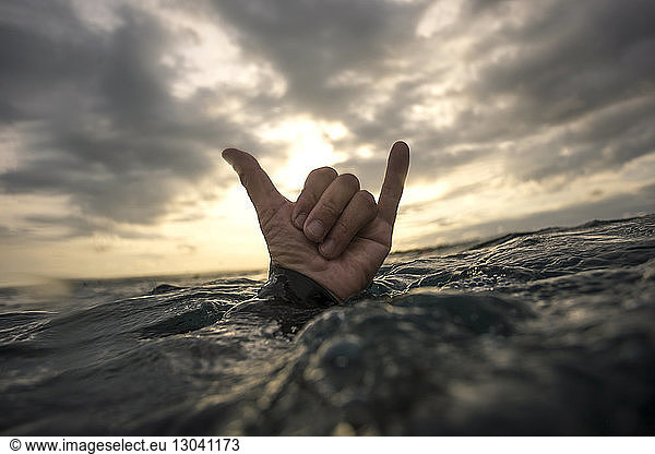 Cropped image of hand showing shaka sign in sea