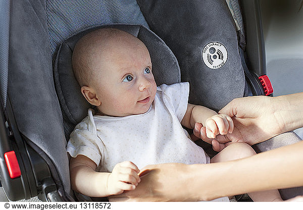 Cropped image of hands holding baby sitting in car seat