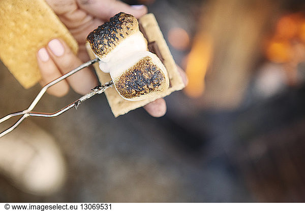 Cropped image of hands holding marshmallow with fork over smores