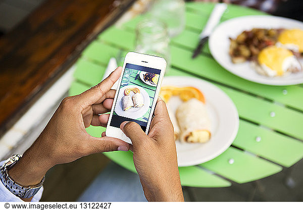Cropped image of hands photographing food served on table