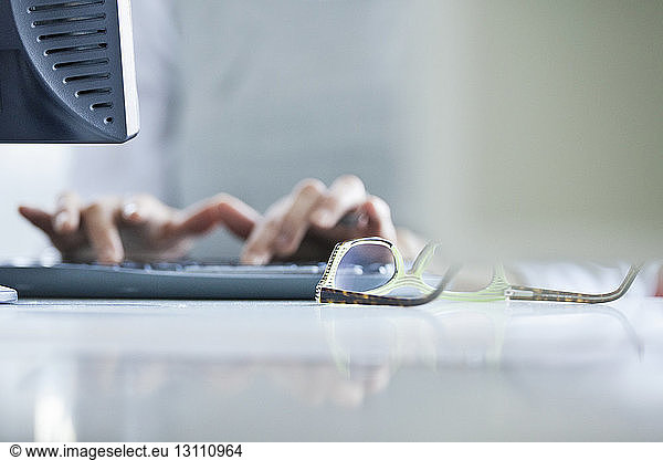 Cropped image of hands using computer by eyeglasses at office desk