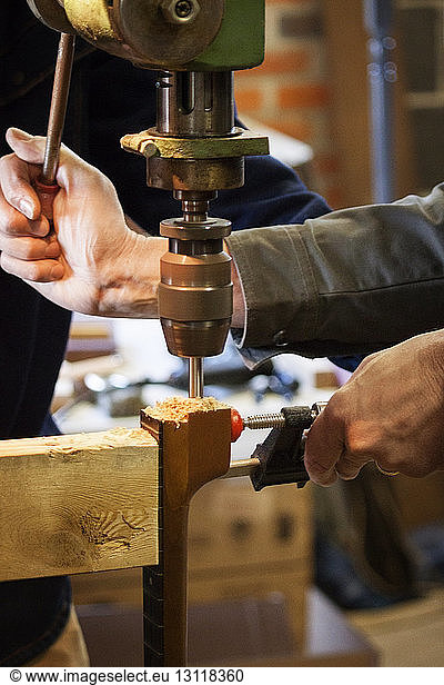 Cropped image of hands using machine to drill wood in workshop