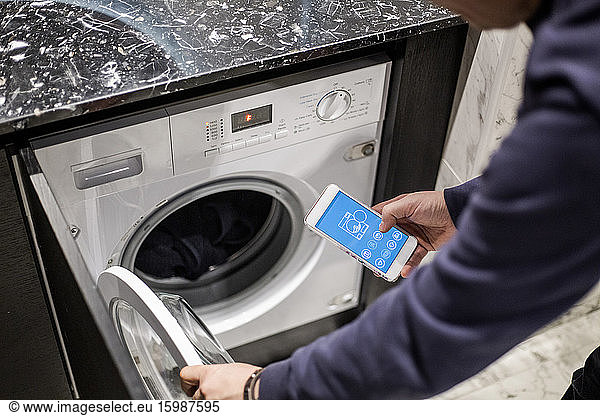 Cropped image of man controlling washing machine with mobile app at smart home