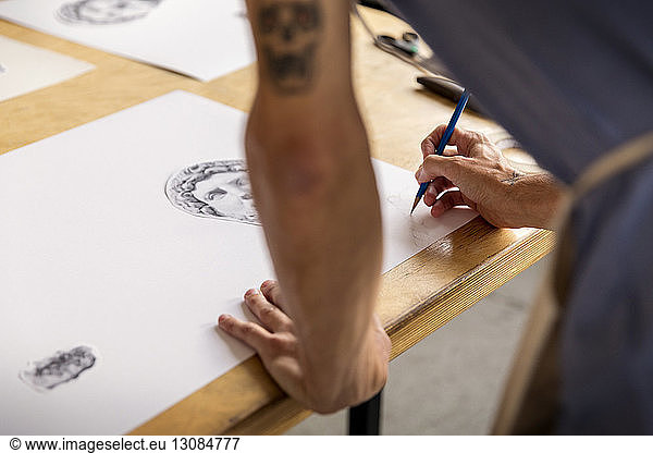 Cropped image of man drawing sketch while standing in workshop