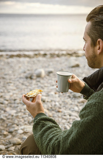Cropped image of man eating snack with coffee at beach