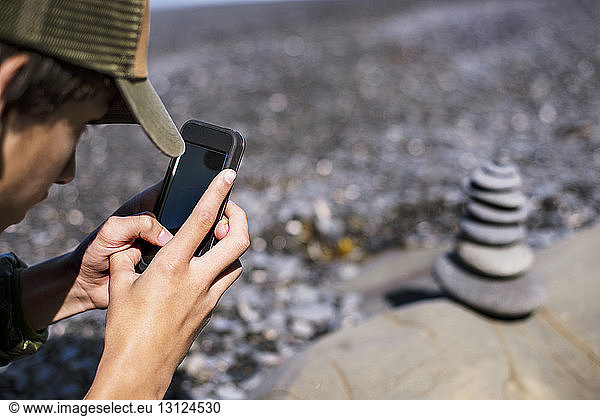 Cropped image of man photographing stack of stones through mobile phone