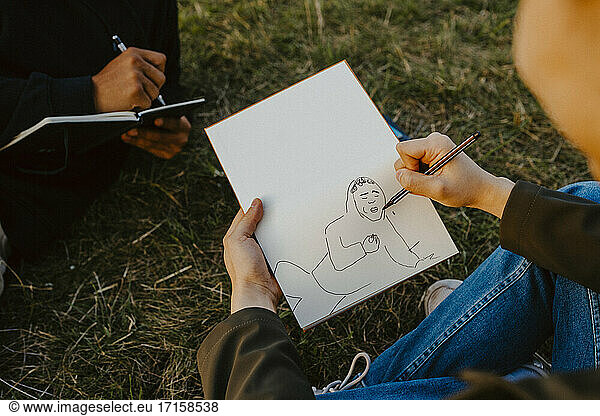 Cropped image of man's hands sketching in book at park