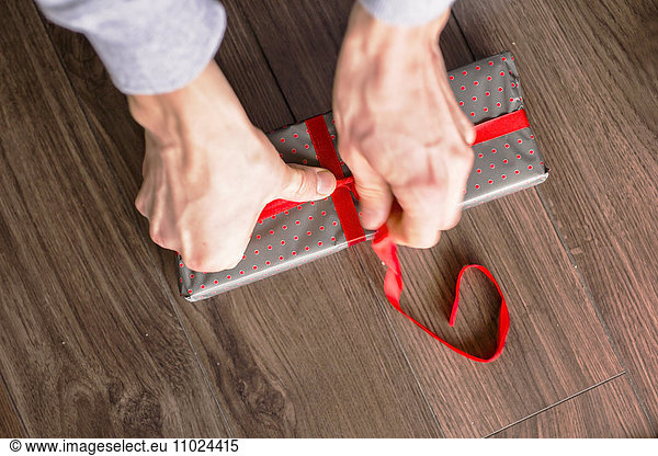Cropped image of man's hands wrapping gift box on hardwood floor