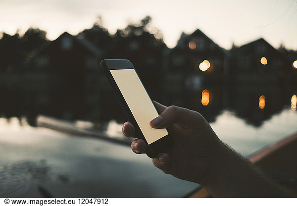 Cropped image of man text messaging through smart phone at lake