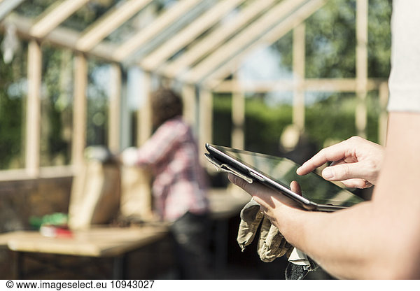 Cropped image of man using digital tablet while woman working in background at greenhouse