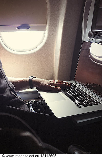 Cropped image of man using laptop while travelling in airplane