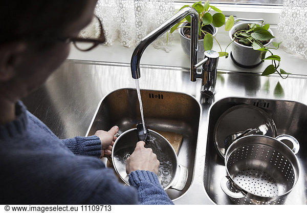 Cropped image of man washing utensils at kitchen sink