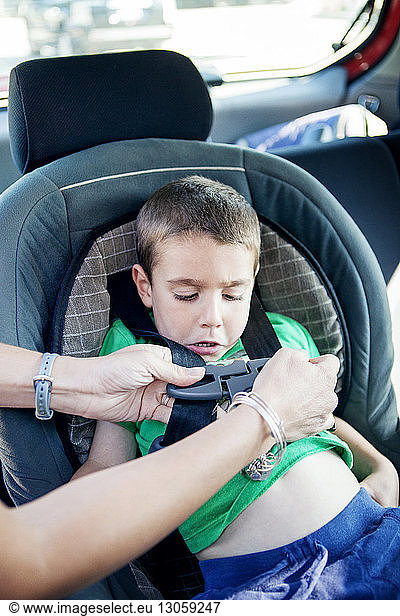 Cropped image of mother fastening seat belt of son's car seat