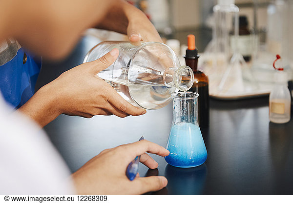 Cropped image of multi-ethnic students mixing solutions at chemistry laboratory in university