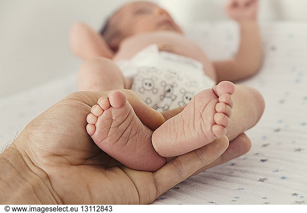 Cropped image of person holding baby's feet on bed