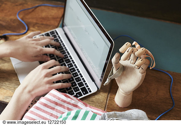 Cropped image of podcaster typing on laptop by hand mannequin with hair elastics at table