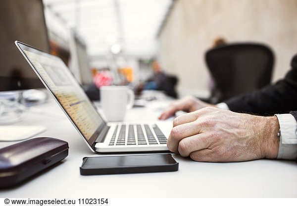Cropped image of senior businessman using laptop at table in creative office