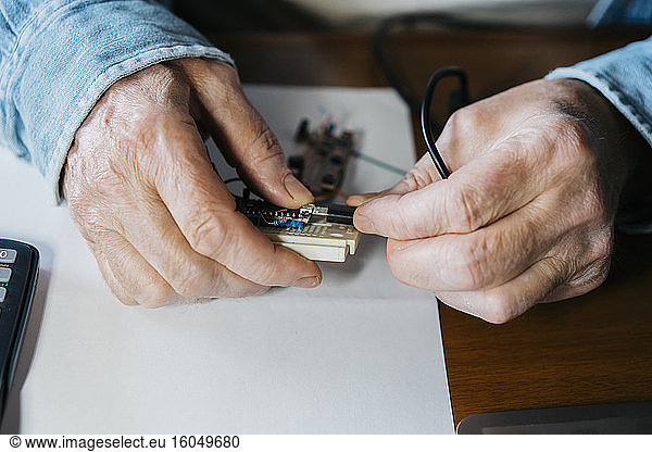 Cropped image of senior man repairing USB board of laptop at home