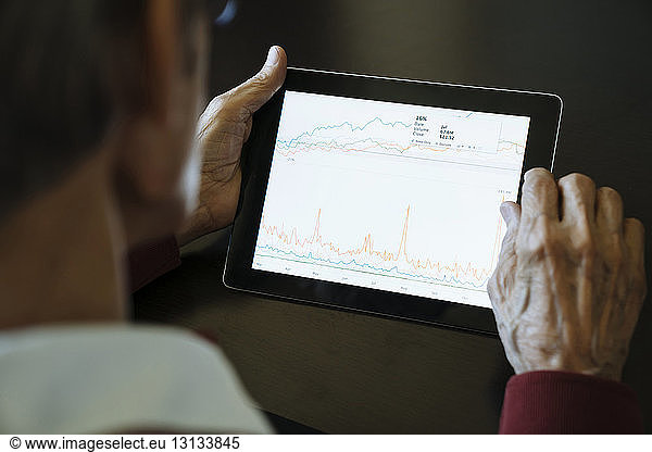 Cropped image of senior man studying graph on tablet computer in financial advisor's office