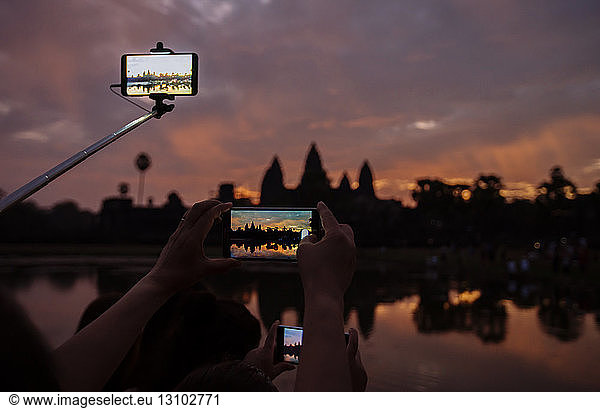 Cropped image of tourists photographing silhouette Angkor Wat temple during sunset